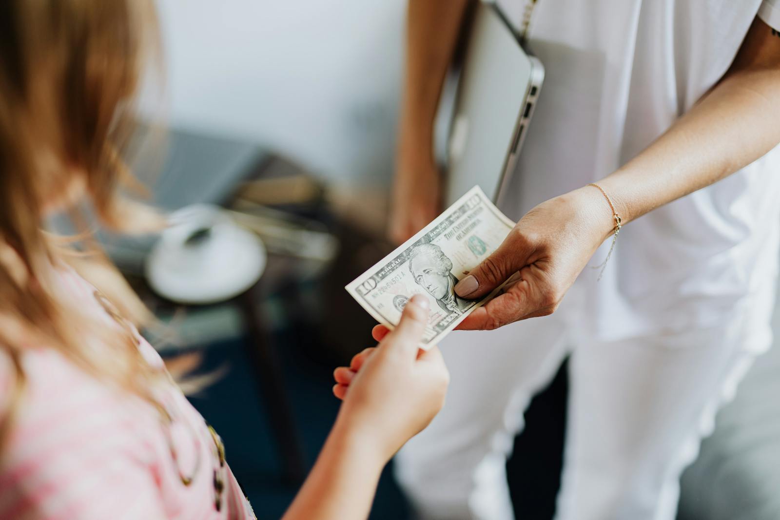 Close-up of a transaction involving a US dollar bill exchanged indoors between two individuals.