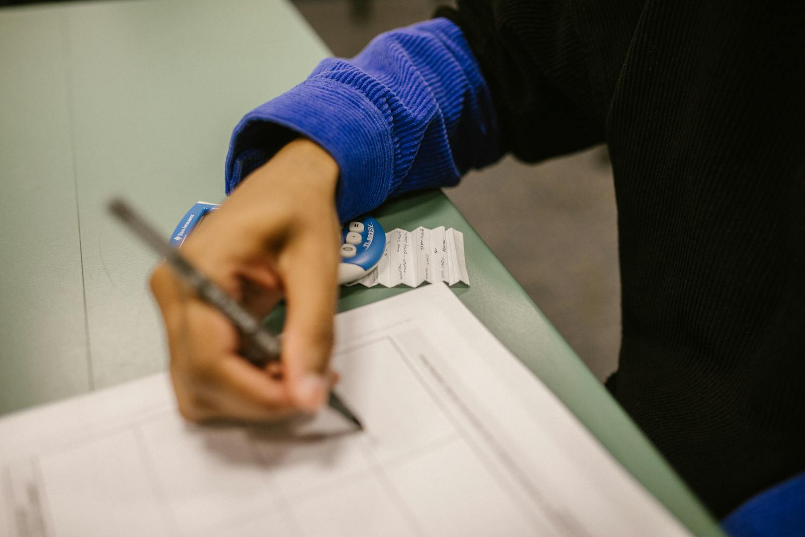 Close-up shot of a student writing on a test paper, hinting at cheating with a note.